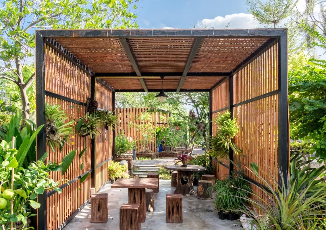 A lush, green garden features one of the elegant wooden garden gazebos surrounded by plants.