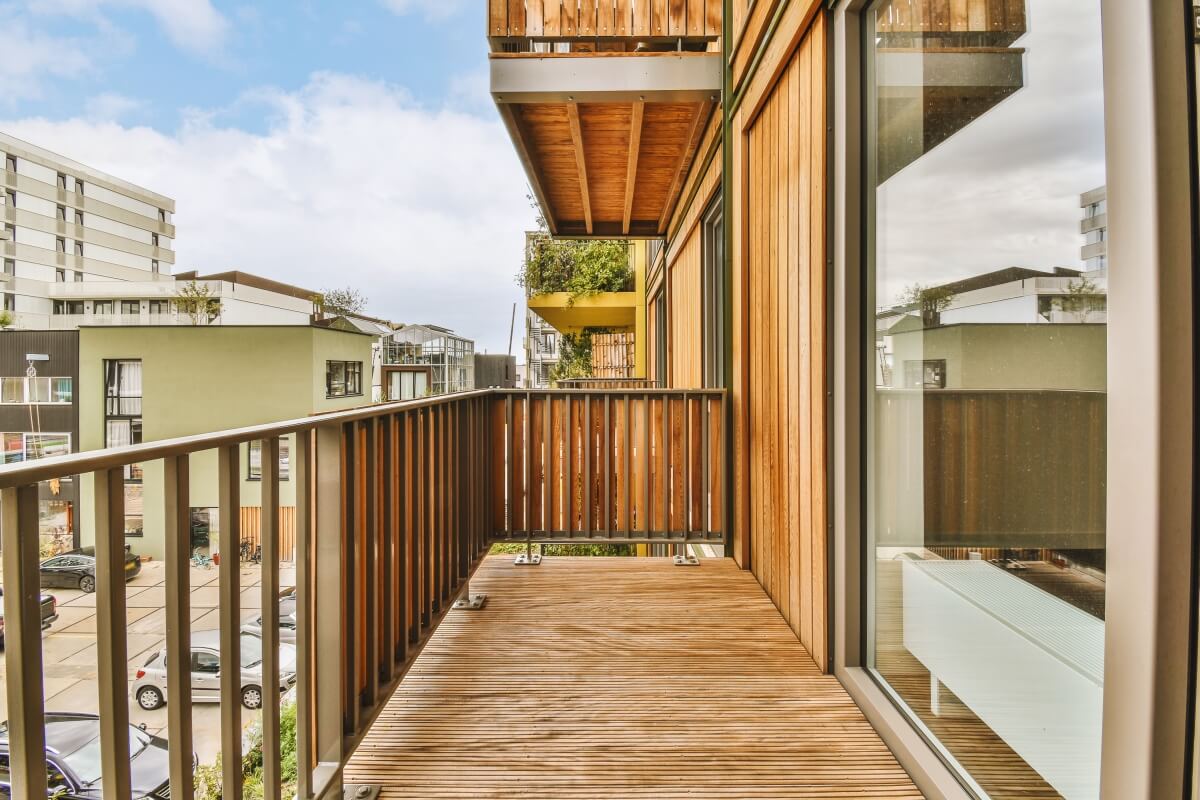 A wooden balcony overlooks modern buildings, featuring a system of movable boards for adjustable railings.